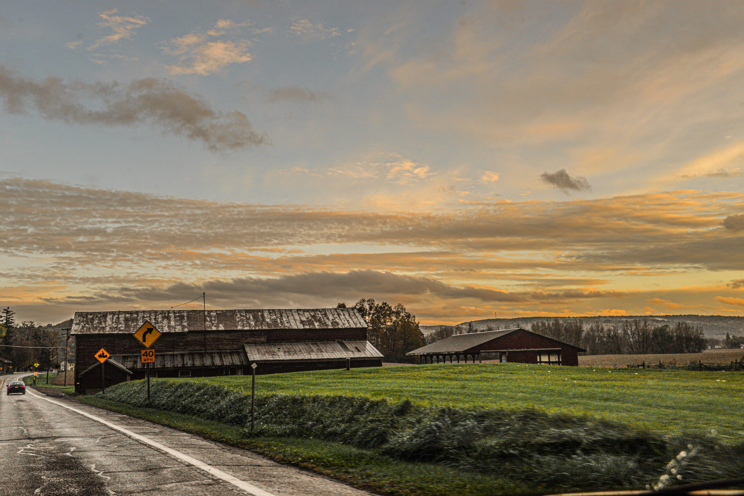 Beutiful sunset over rural highway with Barns on side of blue highway by Franklin Crawford