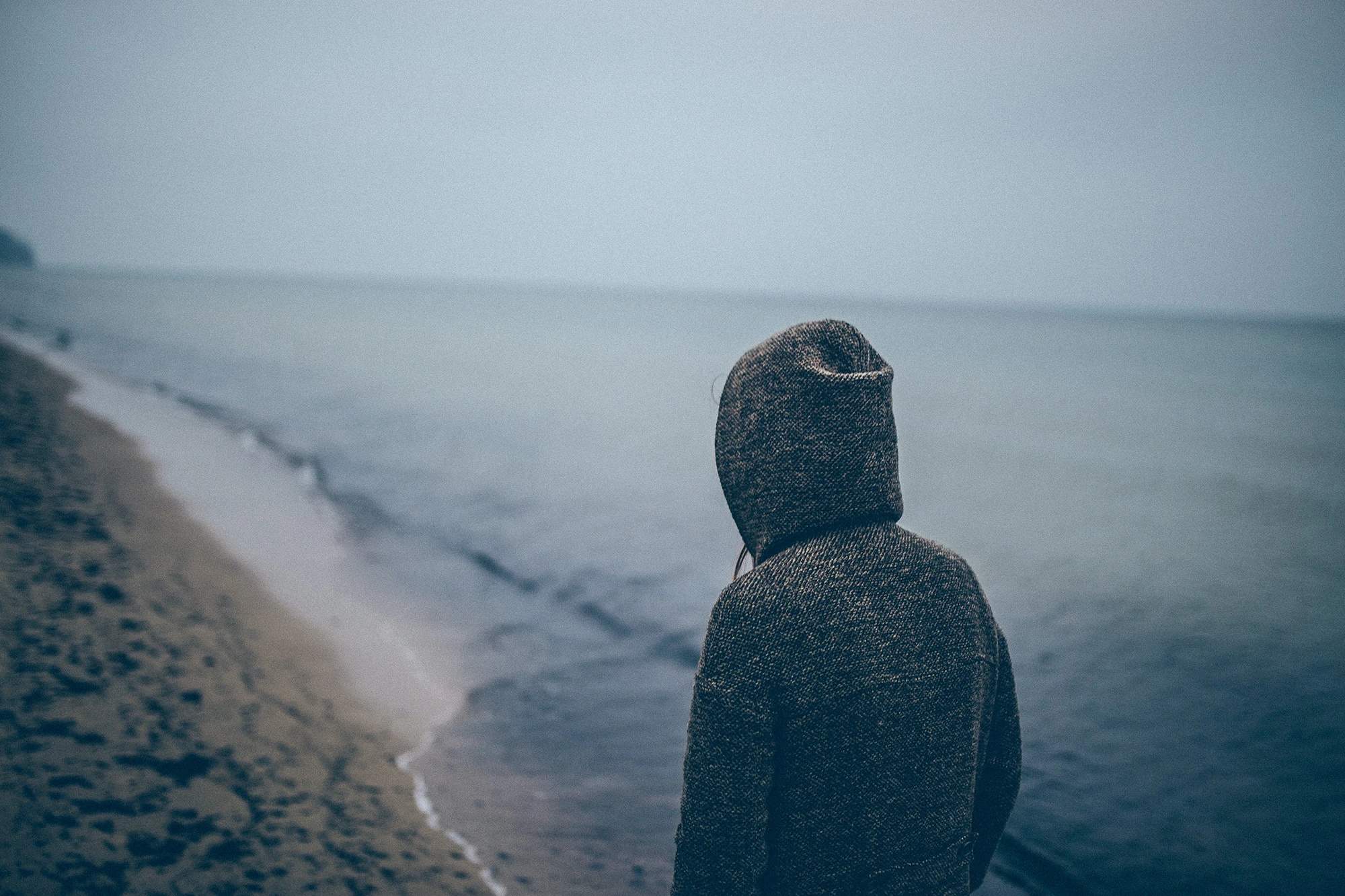 man in a blue hoodie swweatshirt on an overlook over the ocean. by Pat on Usplash.