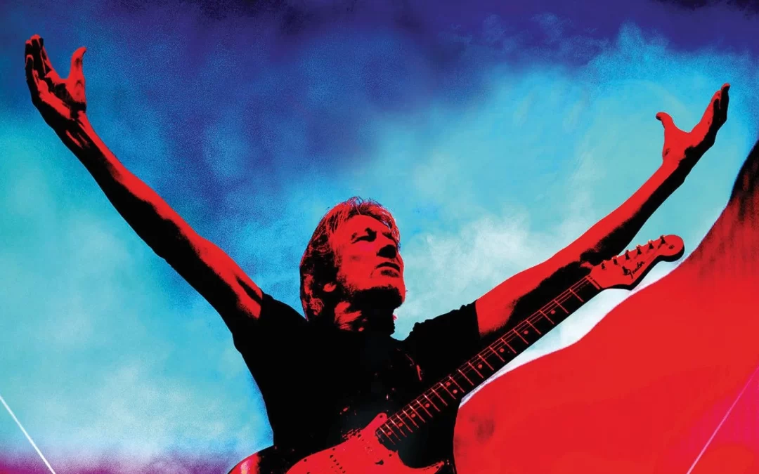 Roger waters bathed in colored stage light against a dramatic background sky