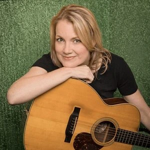 Kelly Willis sitting in chair with Acoustic guitar on lap wearing black t shirt